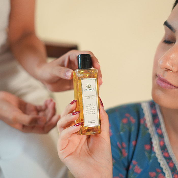 Woman holding and looking at hair oil bottle image on padma gallery page