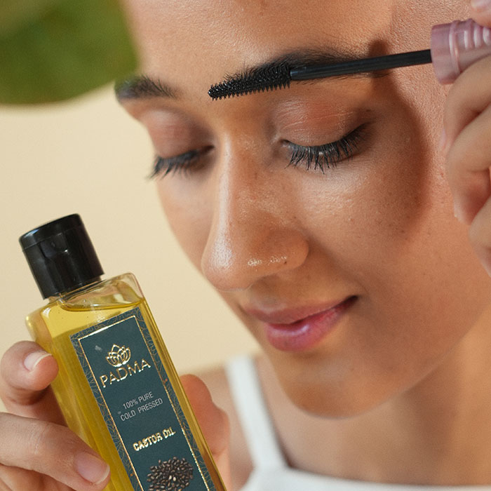 Woman applying mascara on her eyebrow and holding castor oil image on padma gallery page